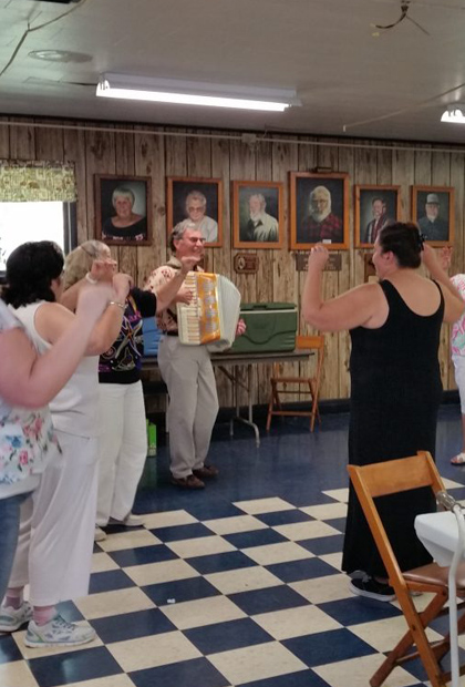 Women playing an accordian while others dance along